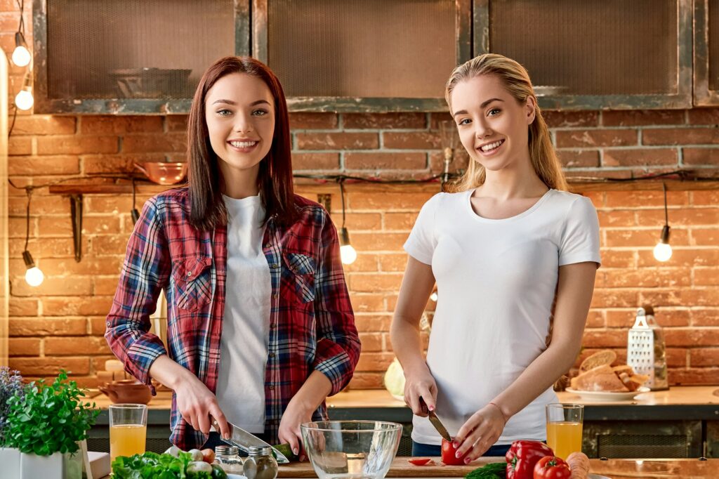 Eat organic for health. Smiling young women cutting vegetables in modern kitchen. Cozy interior